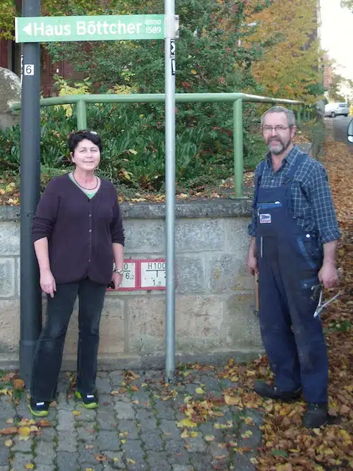 Elvira Böttcher und Karl-Christian Köhler vor einem der neuangebrachten Hinweisschilder von „Haus Böttcher – Marsbergs Haus der Geschichte“ in Obermarsberg (Foto: Marsberger Geschichten - Schlüssel zur Vergangenheit e.V.).