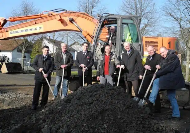 Vollzogen den Spatenstich zum Bau des neuen Feuerwehrgerätehauses in Lippe: Löschzugführer Jens Wildfeuer, Waldemar Herr, Tobias Klein, Leiter der Feuerwehr Burbach, Bauunternehmer Rüdiger Sahm, Bürgermeister Christoph Ewers und die beiden zuständigen Fachbereichsleiter Thomas Leyener und Jochen Becker. Im Bagger sitzend Wolfgang Fey (Foto: Gemeinde Burbach).