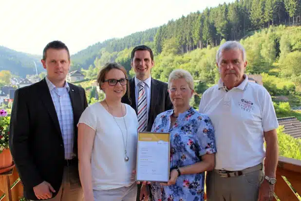 Birgit und Helmut Rauterkus (vorne rechts) freuen sich über die Auszeichnung als „Vier Sterne Ferienwohnung“, welche Bürgermeister Christian Pospischil (Mitte), Amtsleiter Frank Burghaus (links) und Anna Schulte vom Stadtmarketing & Tourismus (vorne links)  dem Ehepaar in Attendorn-Lichtringhausen überbrachten (Foto: Hansestadt Attendorn).