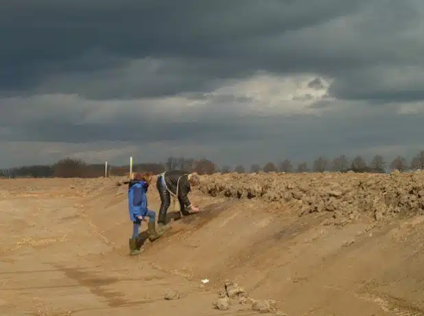 Dr. Eva Cichy und Norbert Reuther M.A. von der Außenstelle Olpe der LWL-Archäologie für Westfalen bei Entdeckung der erster Gruben (schwarze Flecken) der neuen Fundstelle in der Wand eines Regenrückhaltebeckens (Foto: LW/Baales).