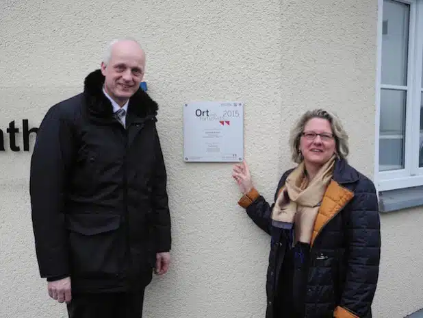 An der Rathauswand hängt die Plakette „Ort des Fortschritts“, die Bürgermeister Christoph Ewers und NRW-Wissenschaftsministerin Svenja Schulze enthüllten (Foto: Gemeinde Burbach).