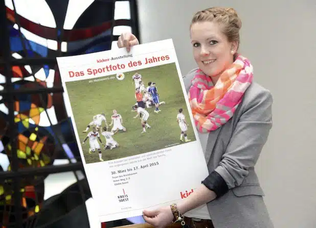 Anna Tüselmann, Auszubildende beim Kreis, zeigt das Plakat, das für die Wanderausstellung „Das Sportfoto des Jahres“ wirbt, die vom 30. März bis 17. April im Foyer des Soester Kreishauses zu sehen ist (Foto: Thomas Weinstock/Kreis Soest).