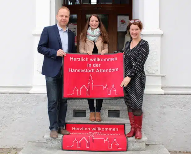 Ronja Wockel von der Hansestadt Attendorn (Bildmitte) überbrachte die ersten Fußmatten an die Attendorner Einzelhändler Nicole Kost (rechts) und Michael Frey (Foto: Hansestadt Attendorn).