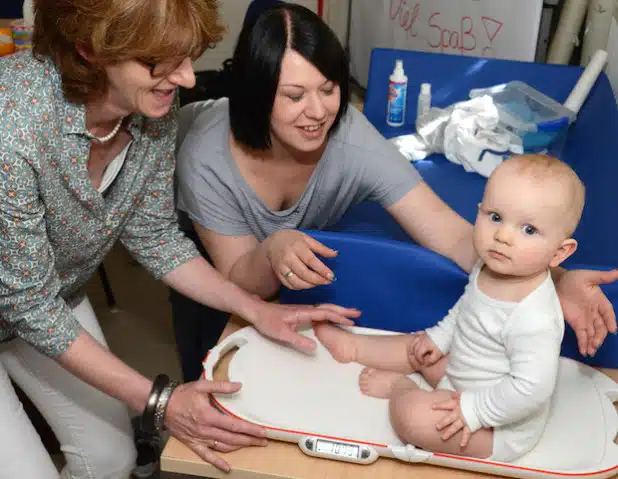 Auch wenn es Linus etwas schwer fällt auf der Waage still zu sitzen, mit der Unterstützung von Mutter Jennifer Straach (2.v.l.) und Familienhebamme Marion Renneker-Beule kann dann doch sein aktuelles Gewicht bestimmt werden (Foto: Judith Wedderwille/Kreis Soest).