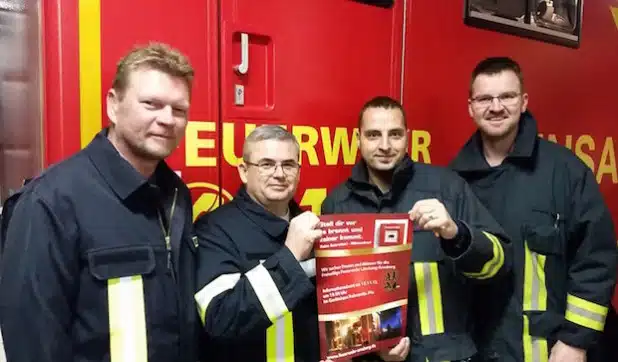 Die Projekt-Verantwortlichen Rolf Hesse und Patrick Beule mit ihren Kameraden José Antonio Martin Delgado und Carlos Borges vom Löschzug Arnsberg mit einem der Veranstaltungsplakate (Foto: Feuerwehr Arnsberg).