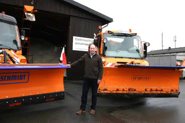 Marc Böhm, Leiter des Integrierten Baubetriebshofes, mit zwei der großen Räumfahrzeuge auf dem Gelände in Enste. Das Salzlager im Hintergrund ist bis zum Rand gefüllt. Nur der Winter fehlt (Foto: Stadt Meschede).